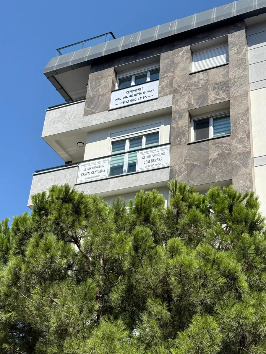 Ağaçların üzerinden görünen bina cephesi ve kat tabelaları